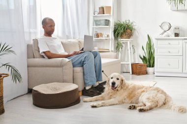 Miyastenia gravis 'i olan Afrikalı bir Amerikalı kanepeye oturmuş evinde Labrador köpeği ile dizüstü bilgisayar kullanıyor..