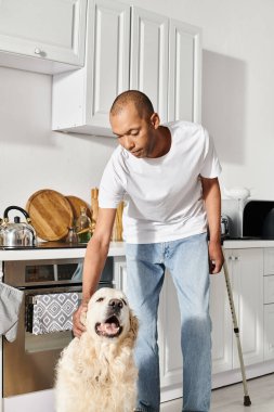 Miyastenia gravis 'i olan Afrikalı Amerikalı bir adam sıcak bir mutfakta Labrador köpeğini kucaklıyor..