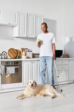 Myasthenia Gravis 'i olan bir Afro-Amerikalı mutfakta elinde baston ve sadık Labrador köpeği ile dikiliyor..