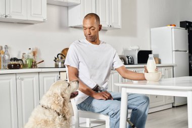 An African American man, disabled, sits at a kitchen table with his loyal Labrador dog, showcasing diversity and inclusion. clipart