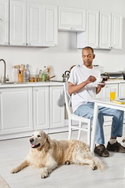 A disabled African American man sitting at a kitchen table with his faithful Labrador dog by his side. clipart