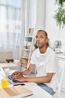 A man of African American descent, living with myasthenia gravis, is engaged in using a laptop computer at a table. clipart