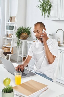 Myastthenia gravis 'i olan engelli bir Afro-Amerikan adam mutfak masasında dizüstü bilgisayar kullanıyor..