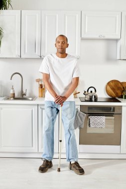An African American man with a cane stands confidently in a kitchen, showcasing strength and resilience. clipart