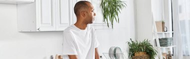 Myastthenia Gravis sendromlu özürlü Afrikalı bir adam mutfakta saksı bitkisinin yanında duruyor..