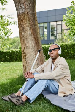 Myastthenia Gravis hastası bir adam bir ağacın altında oturmuş kulaklıkla müzik dinliyor.