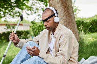 An African American man with myasthenia gravis syndrome relaxes on grass with headphones, embracing the music. clipart