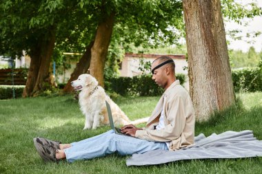 A diverse man with Myasthenia Gravis sits on the grass, using a laptop while accompanied by his loyal Labrador dog. clipart