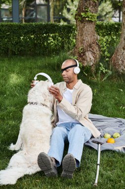 An African American man with myasthenia gravis sits with his Labrador dog in the grass, both enjoying music through headphones. clipart