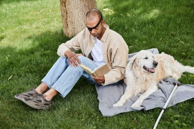 An African American man with Myasthenia Gravis syndrome reading a book on a blanket with his Labrador dog. clipart