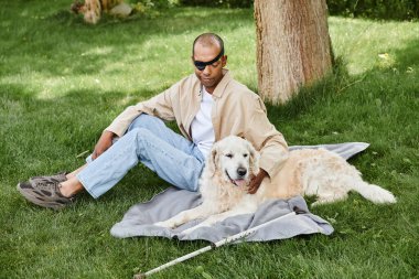 Myastthenia Gravis 'i olan bir adam çimenlerde oturur, iki köpeğiyle yansıtır, çeşitlilik ve kapsama gösterir..