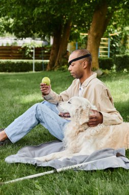 Miyastenia gravis sendromlu bir Afrikalı Amerikalı sadık Labrador köpeğiyle çimlerde oturuyor..