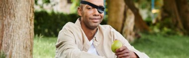 A blindfolded African American man holds an apple, symbolizing diversity and inclusion in society. clipart