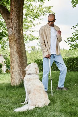 A disabled African American man with myasthenia gravis syndrome standing next to a Labrador dog on a vibrant green field. clipart