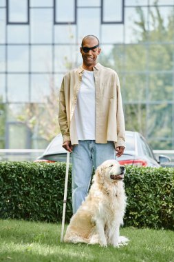 Özürlü bir Afrikalı Amerikalı adam yemyeşil bir alanda Labrador köpeğinin yanında duruyor. Uyum ve kapsayıcılığı simgeliyor..