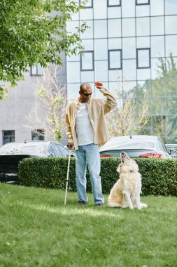 Miyastenia gravis 'i olan Afro-Amerikalı bir adam yemyeşil bir alanda Labrador köpeğinin yanında duruyor..