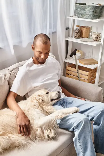 ラブラドールの犬とソファーでリラックスして 多様性と包摂を示すミスタシアグラビスを持つ男 — ストック写真