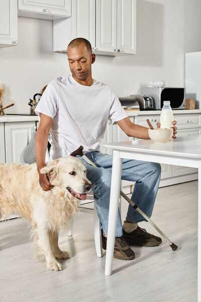 A disabled African American man shares a quiet moment at a kitchen table with his loyal Labrador dog.