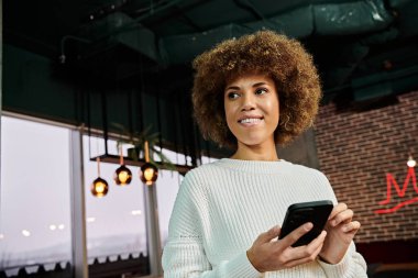 Modern bir kafede elinde akıllı telefon tutan şık bir Afrikalı Amerikalı kadın..