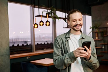 man browses his cell phone while standing in a modern restaurant clipart