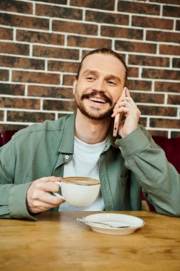 Bir adam, modern bir kafe ortamında telefon görüşmesi yapmak için masada oturuyor..