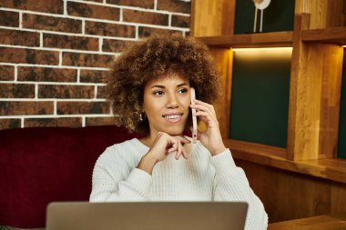 Bir Afro-Amerikalı kadın modern bir kafede oturuyor, laptopuna dalmış..