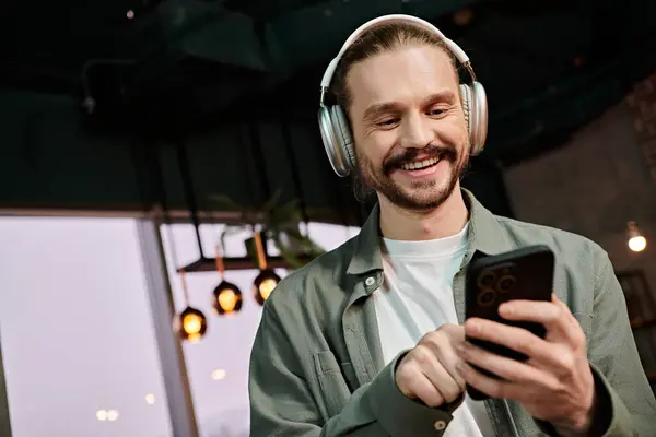stock image A man, headphones on, holding a cell phone, lost in music and conversation in a modern cafe setting.