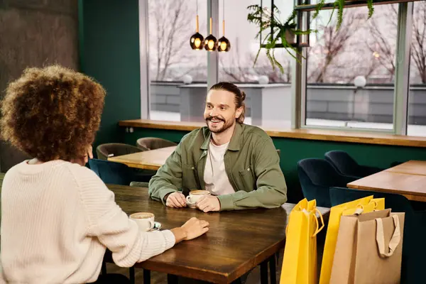 ある男性とアフリカ系アメリカ人の女性が近代的なカフェのテーブルに座り つながりの瞬間を共有しながら会話をしました — ストック写真