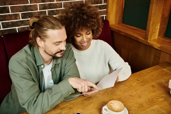 stock image An African American woman and man sit at a table, choosing meal in menu in a modern cafe.