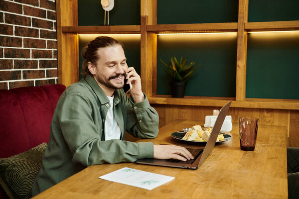 Мужчина, сидящий за столом в современном кафе, погружен в телефонный разговор.