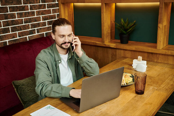 Мужчина сидит за столом, разговаривает по мобильному телефону в модном современном кафе.