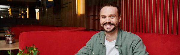 A man relaxes on a vibrant red couch in a modern cafe, taking in his surroundings.