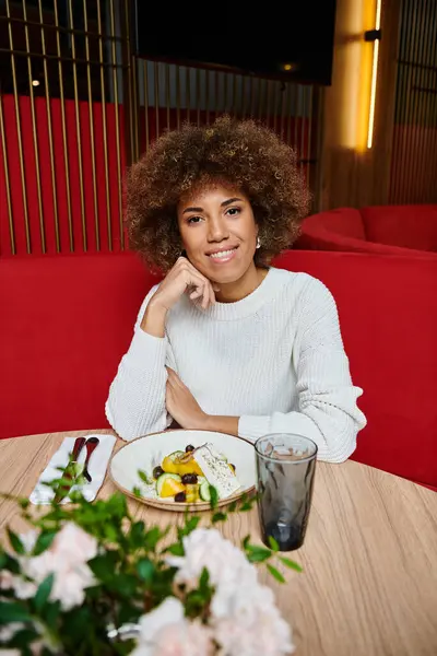 一位时髦的非洲裔美国女人坐在餐桌旁 一边在现代咖啡馆里享用着一盘美味的食物 一边沉思着 — 图库照片