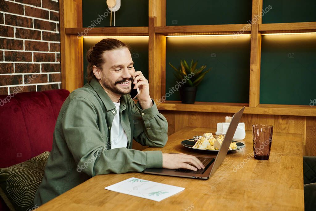 A man, seated at a table in a modern cafe, is engrossed in a phone conversation.