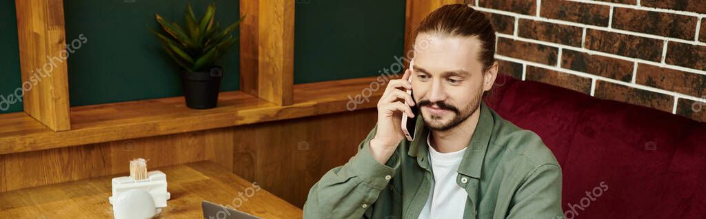 A man sitting on a couch, engrossed in a conversation on a cell phone.