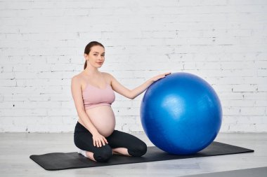 Yoga yapan hamile kadın, egzersiz topuyla mindere poz veriyor.