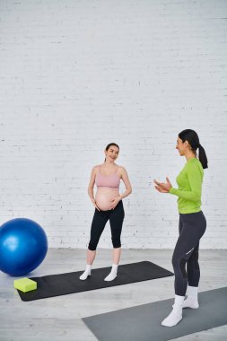 Hamile bir kadın doğum öncesi kursunda koçunun rehberliğinde mavi bir topla yoga yapıyor..