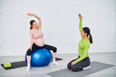 Hamile kadın koçunu takip ediyor, veli kursları sırasında egzersiz topları üzerinde yoga pozları veriyor..