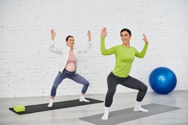 Hamile kadın nazikçe yoga yapıyor, ebeveyn kursu sırasında eğitmeninin rehberliğinde..
