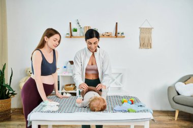 A young beautiful mother lovingly stands next to her baby on a bed while receiving guidance from a parent coach. clipart