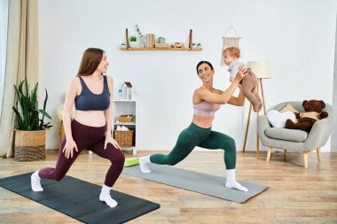 Genç bir anne ve bebeği, bir koçun rehberliğinde oturma odalarında yoga yapıyorlar..