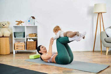 Genç ve güzel bir anne, ebeveynlik kursunda koçun rehberliğinde bebeğiyle yoga yapıyor..