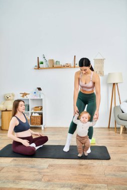 Genç bir anne, ebeveyn kursunda koçu tarafından rehberlik edilirken bebeğiyle birlikte yoga yapıyor..