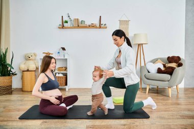 Genç ve güzel bir anne, ebeveynlik kursundan koçu tarafından rehberlik edilen bebeğiyle yoga yapıyor..