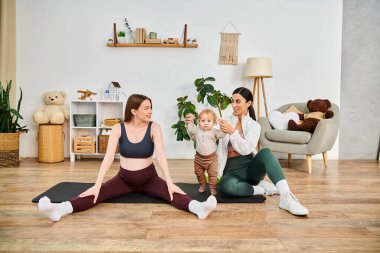 A young beautiful mother sits on a yoga mat, cradling her baby, with the guidance of her coach at parents courses. clipart