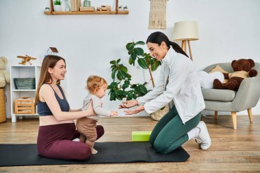 Genç, güzel bir anne ve bebeği, ebeveyn kursunda öğretmenlerinin rehberliğinde huzurlu bir yoga seansına giriyorlar..