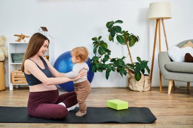 Güzel, genç bir anne yoga minderinde oturuyor, anne ve babasının rehberliğinde bebeğini kucağına alıyor..