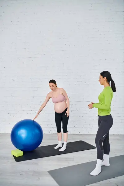 妊娠中の女性は 親コースのトレーニングセッション中にバランスをとる青い運動ボールの隣に立っています — ストック写真