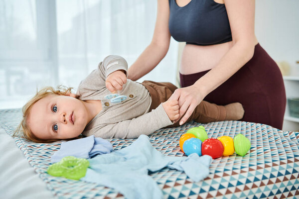 A baby lays peacefully on a bed next to a caring woman. The young mother is attentively watching over her child with love.