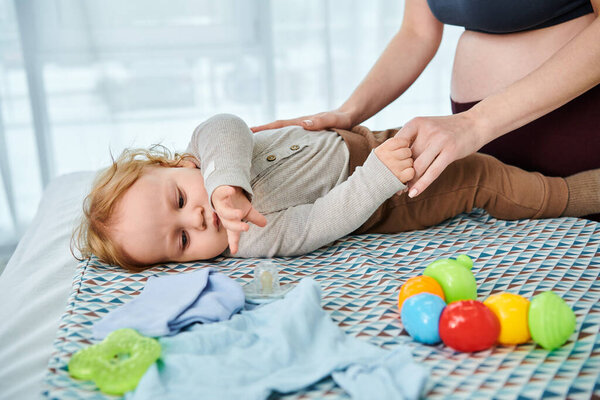 Серенький момент, когда молодая красивая мать любовно собирает ребенка, лежащего рядом с ней на кровати дома.